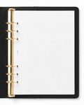 A black leather-bound ring binder  notebook with gold metal rings and a Notairé white dotted page insert, shown from a top-down view on a white background.