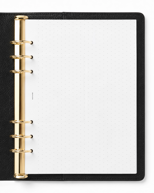 A black leather-bound ring binder  notebook with gold metal rings and a Notairé white dotted page insert, shown from a top-down view on a white background.