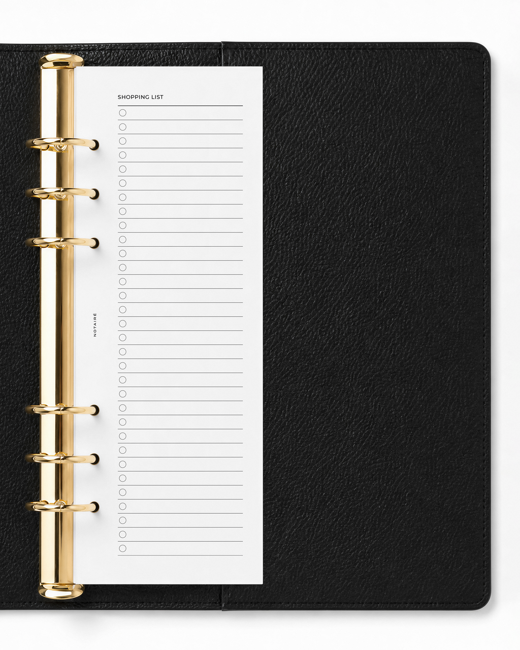 A black textured ring binder planner shown open, featuring a white half-page A5 Notairé insert with a shopping list template and gold-tone metal rings.