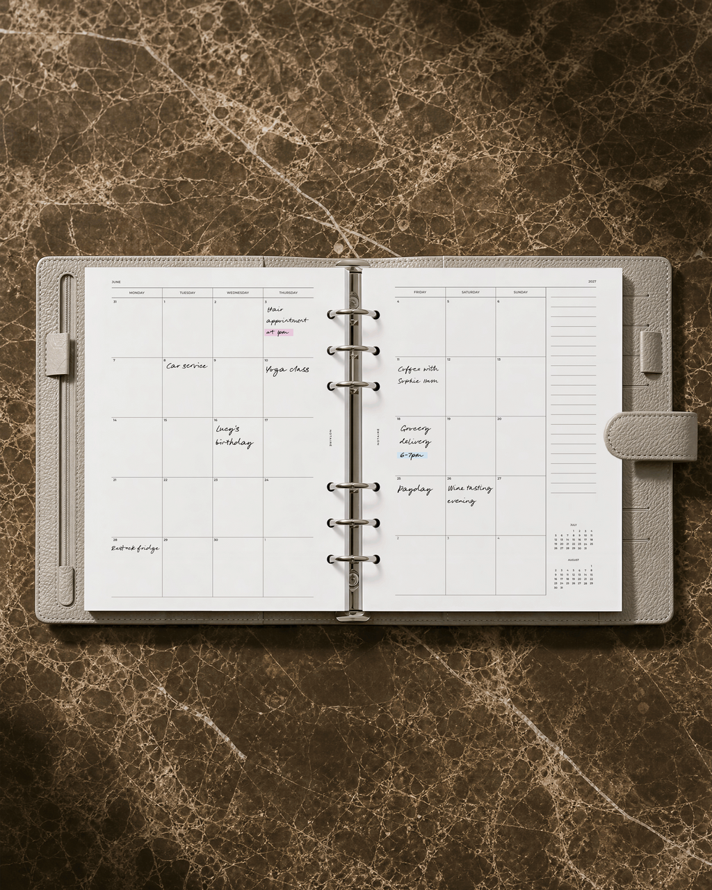 An open Filofax ring-bound planner with a Notairé monthly calendar layout and handwritten notes, displayed on a brown marble-textured background.